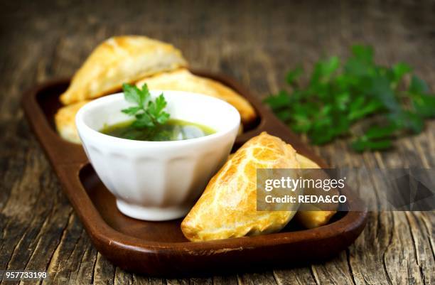 Empanadas with chimichurri sauce on wooden table.