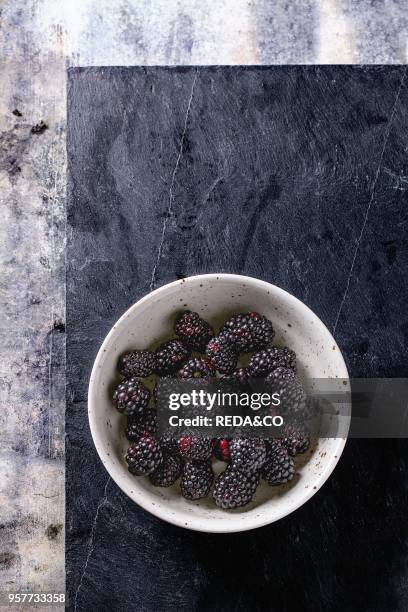 Spotted white ceramic bowl of blueberries at black slate board over old tin background. Top view.