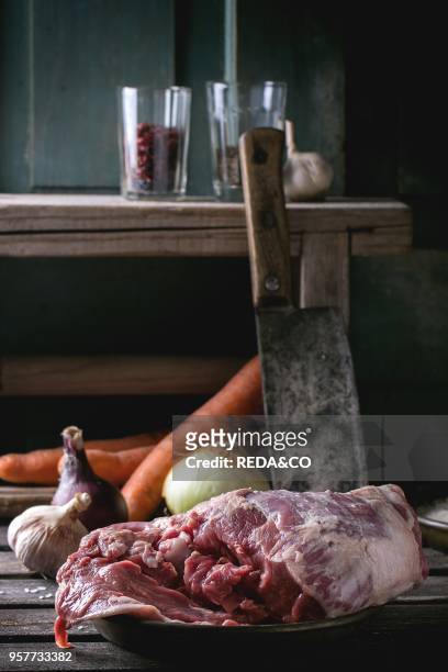 Raw loaf of lamb with vegetables and old meat backsword over wooden table. Dark rustic style.