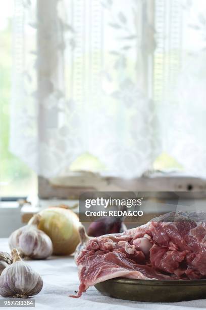 Raw loaf of lamb with onions over white kitchen table. With window as background. Rustic style.