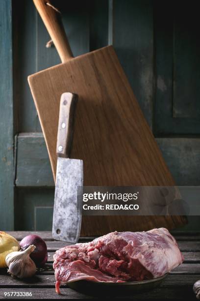 Raw loaf of lamb with vegetables and old meat backsword over wooden table. Dark rustic style.