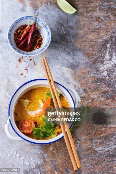 White Ceramic pan with Spicy Thai soup Tom Yam with Coconut milk, Chili pepper and Shrimp over gray stone background. With wooden chopsticks. Top...