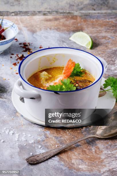 White Ceramic pan with Spicy Thai soup Tom Yam with Coconut milk, Chili pepper and Seafood over gray stone background.