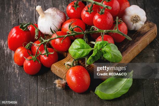 Assortment of colorful cherry tomatoes with garlic and basi on small cutting board over old wooden table.