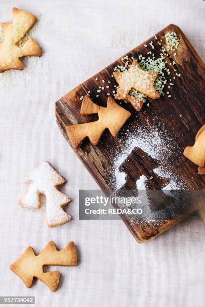 Shortbread Christmas cookies for cups in sugar powder and small cutting board over table with white tablecloth. Top view. Shape as Christmas tree,...