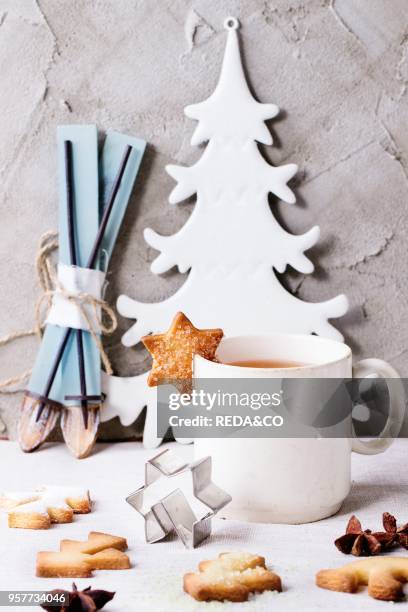 Shortbread Christmas cookies for cups, vintage cup of hot tea, cookie cutter and sugar powder over table with white tablecloth with Christmas decor...