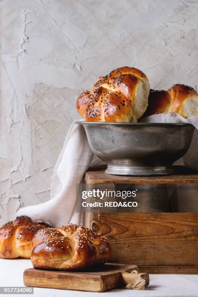 Heap of sweet round sabbath challah bread with white and black sesame seeds in vintage metal bowl on wooden chest and on small cutting board over...