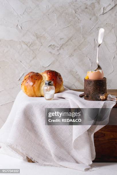 Breakfast with started eating soft-boiled egg with pouring yolk in wooden eggcup and home made bread served with salt and silver spoon on wooden...