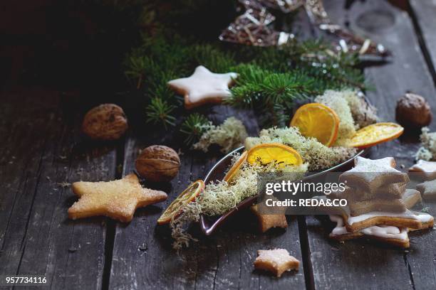 Christmas glazed star shapes cookies with Christmas tree, moss and dry sliced orange in ceramic plate over red wooden table. Dark rustic style, day...