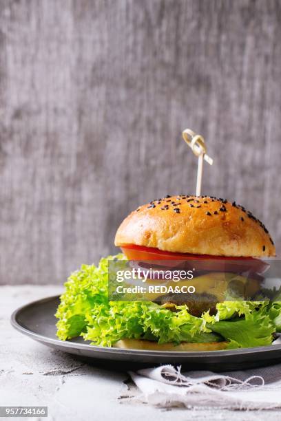 Fresh homemade hamburger with black sesame seeds in vintage metal plate, served over white plastered table and white textile with gray wooden...