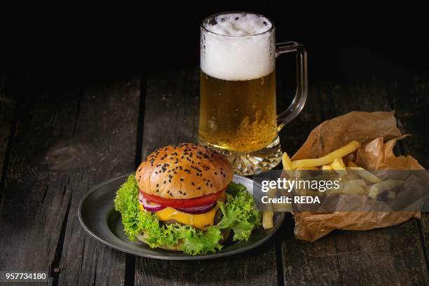 Fresh homemade burger with in old metal plate with french fries potatoes in baking paper, served with glass of cold lager beer over old wooden table...