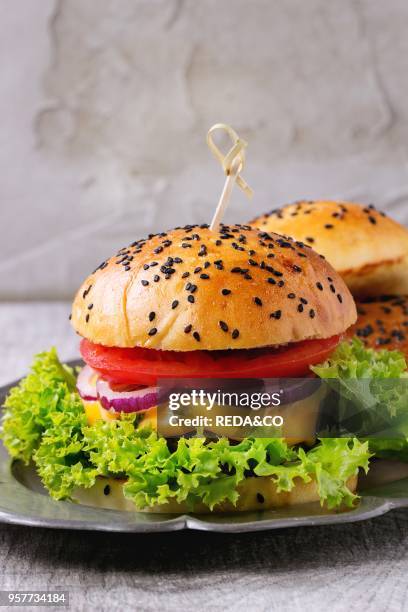 Fresh homemade burger with black sesame seeds in vintage metal plate, served over gray wooden table. Rustic style.