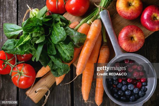 Assortment of fresh fruits, vegetables and berries. Bunch of carrots, spinach, tomatoes and red apples on chopping board, blueberries and cranberries...