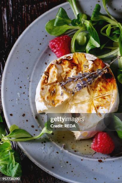 Melting sliced grilled goat cheese on blue plate, served with liquid honey, lavender, raspberries, wholegrain toast and green salad. Over old wooden...