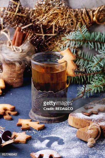 Shortbread Christmas cookies for cups in sugar powder, glass of hot tea in cup holder on table with blue tablecloth. Christmas decor at background....