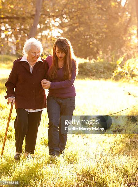 young woman helping older women walk in woods - grandma cane stock pictures, royalty-free photos & images