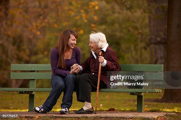 older woman and young woman holing hands on bench - young woman and senior lady in a park stock pictures, royalty-free photos & images