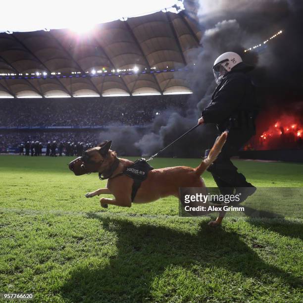 Police dog is seen on the pitch as fans throw flares during the Bundesliga match between Hamburger SV and Borussia Moenchengladbach at...