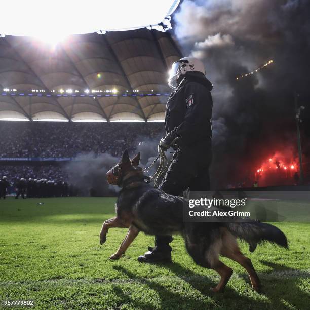 Police dog is seen on the pitch as fans throw flares during the Bundesliga match between Hamburger SV and Borussia Moenchengladbach at...