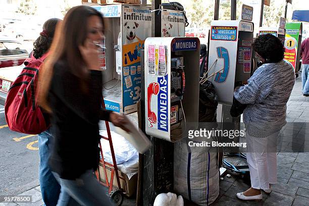 People use Telmex phone booths as a woman passes by on her mobile phone in Mexico City, Mexico, on Thursday, Jan. 14, 2010. Carlos Slim's America...