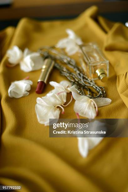perfume bottle, red lipstick and a necklace on a yellow background with white orchid petals - white lipstick stock-fotos und bilder