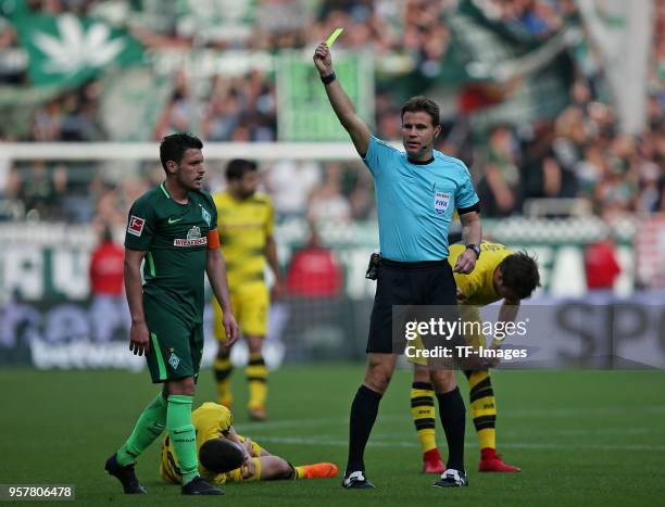 Referee Dr. Felix Brych shows a yellow card to Zlatko Junuzovic of Bremen and Christian Pulisic of Dortmund lays on the ground during the Bundesliga...