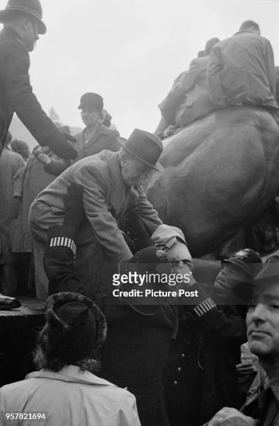 Two policemen helping an elderly man down from one of the bronze lions in Trafalgar Square, during celebrations of the wedding of Princess Elizabeth...