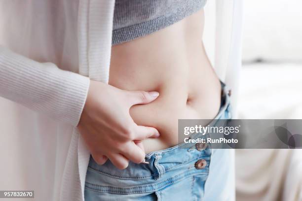 woman pinching fat on abdomen - femme main ventre photos et images de collection