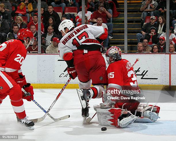 Jimmy Howard of the Detroit Red Wings makes a save as teammate Drew Miller ties up Rod Brind'Amour of the Carolina Hurricanes during an NHL game at...