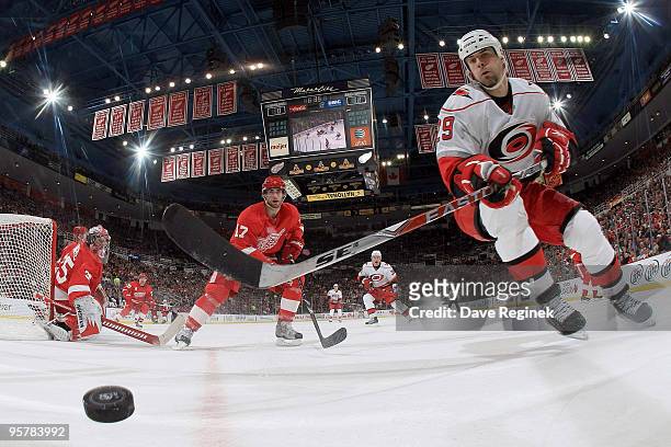 Tom Kostopoulos of the Carolina Hurricanes reaches for the puck defended by Patrick Eaves of the Detroit Red Wings as goalie Jimmy Howard watches the...