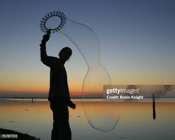 silhouette of a man blowing a large soap bubble - big bubble stock-fotos und bilder