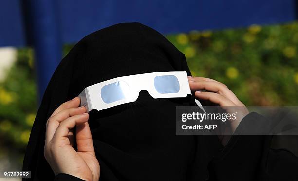 Saudi woman uses tinted glasses to watch a partial solar eclipse in the port city of Jeddah on November 15, 2010. An annular eclipse raced across...