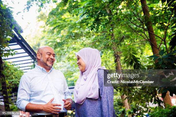 muslim lady laughing with her male friend in a garden - two elderly friends chatting in a community park stock pictures, royalty-free photos & images