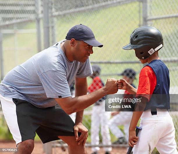 coach bumping fists with little league batter - baseball kid stock-fotos und bilder