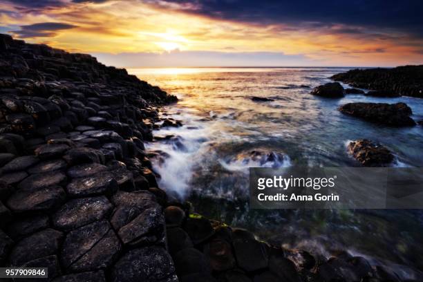 sunset over basalt columns forming famous giant's causeway in northern ireland, long exposure - bushmills stock pictures, royalty-free photos & images