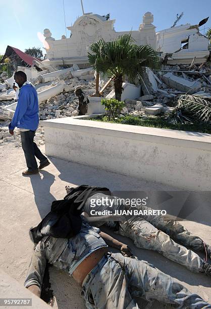Man covers his nose and mouth as he walks next to bodies lying outside the collapsed Palace of Justice , in Port-au-Prince, on January 14 following...