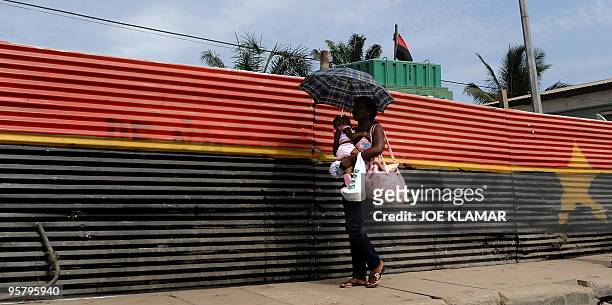 Woman carries a baby along a fence painted as an Angolan flag in one of the streets in Angola's capital of Luanda on January 13, 2010.Angola hosts...