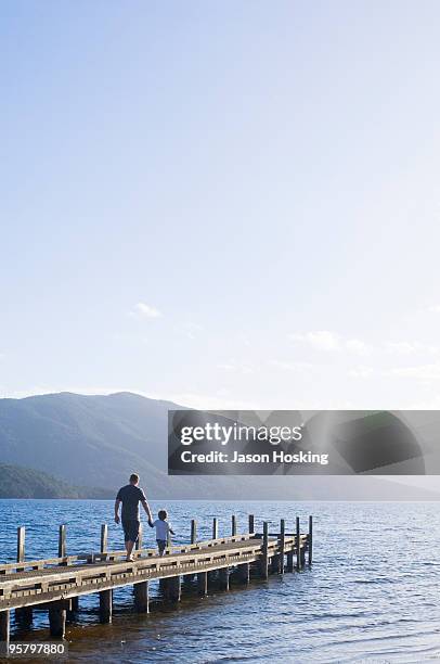 young boy walking with his father on lake jetty - contraluz fotografías e imágenes de stock