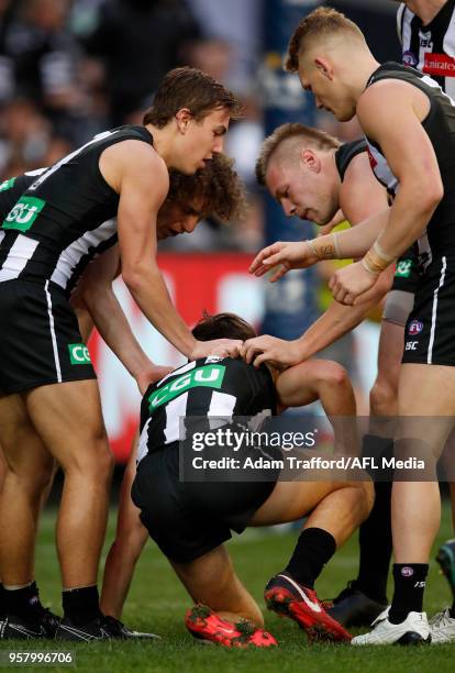 Tom Phillips of the Magpies is checked on by teammates after being hit in the head kicking a goal by the knee of teammate Chris Mayne of the Magpies...