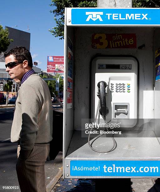 Pedestrian stands next to a Telmex phone booth in Mexico City, Mexico, on Thursday, Jan. 14, 2010. Carlos Slim's America Movil SAB, the largest Latin...