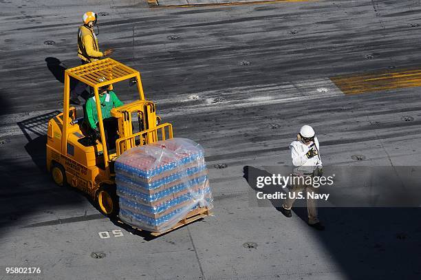 Sailors aboard the Nimitz-class aircraft carrier USS Carl Vinson move pallets of relief supplies as the ship arrives January 15, 2010 off the coast...