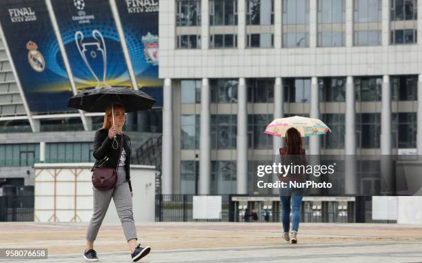 Women under the umbrellas walk past NSC Olimpiyskiy Stadium covered with banners for the Champions League in Kyiv, Ukraine, May 13, 2018. Kyiv...