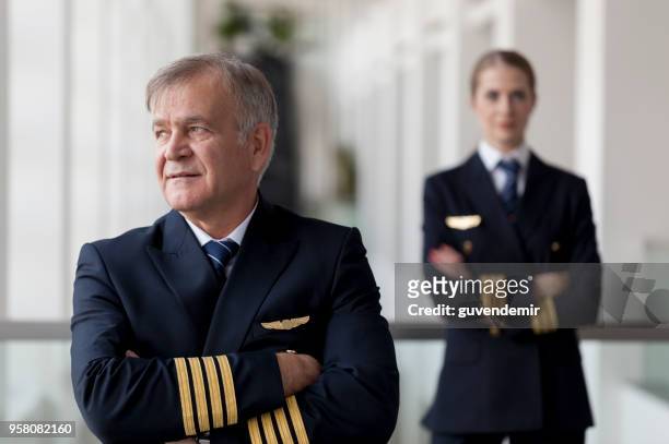 brazos doblados capitán senior y su copiloto femenina - co pilot fotografías e imágenes de stock