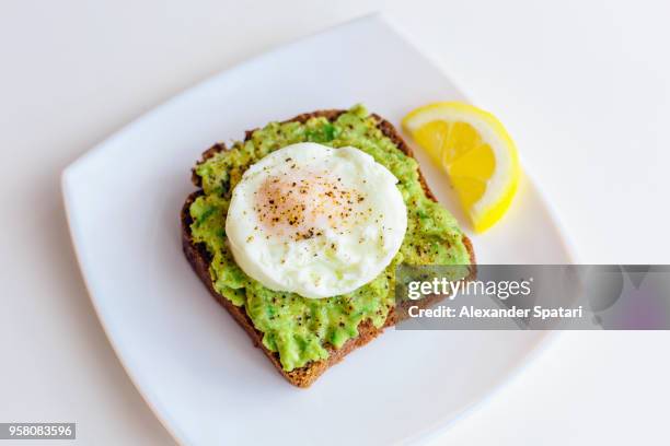 homemade avocado toast with rye bread, egg on top and slice of lemon - avocado toast stock pictures, royalty-free photos & images