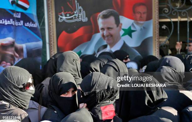 Syrian women walk past a large portrait of President Bashar al-Assad and a watermarked portrait of his late father and former President Hafez...