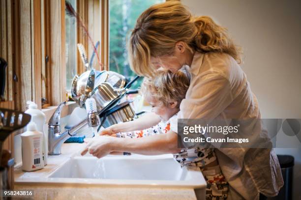mother assisting son in washing hands at kitchen sink - child washing hands stockfoto's en -beelden