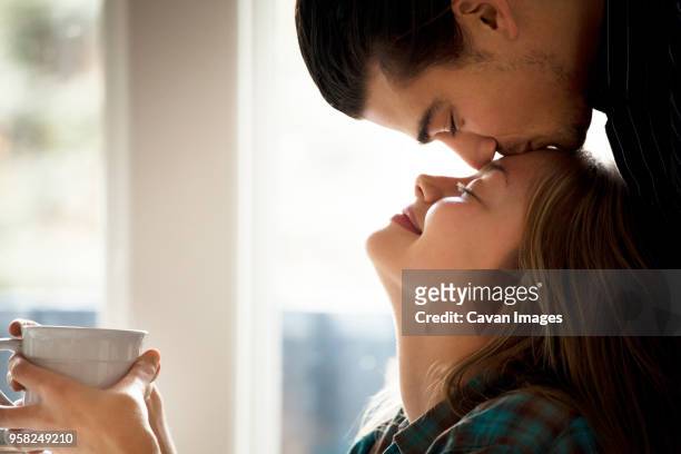 man kissing girlfriend on forehead at home - forehead stock-fotos und bilder