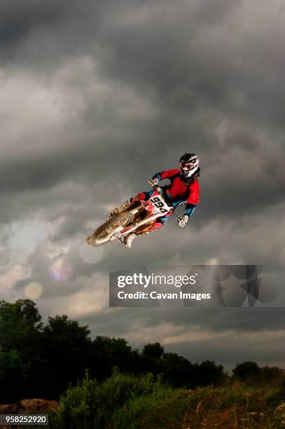 low angle view of biker performing stunt in mid-air against cloudy sky - motorcycle stunt stock pictures, royalty-free photos & images
