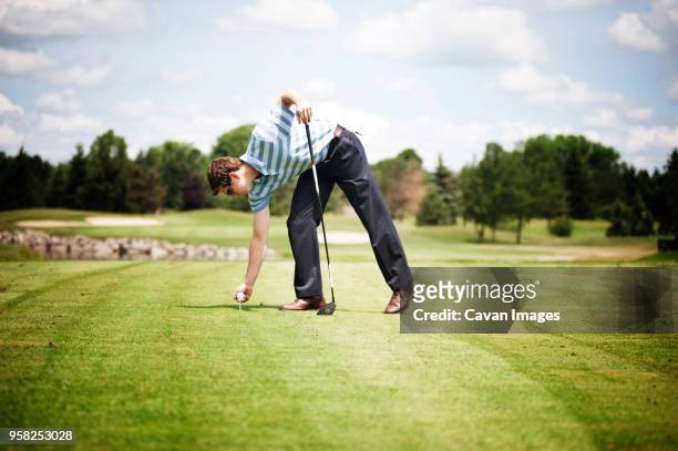full length of man placing ball on tee at golf course - bent golf club stock pictures, royalty-free photos & images