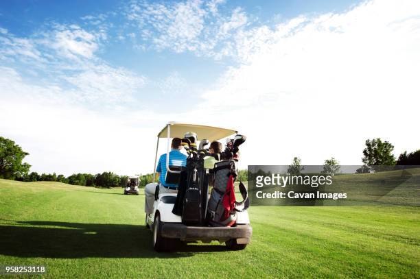 rear view of friends riding in golf cart in field against sky - golf bag stock pictures, royalty-free photos & images